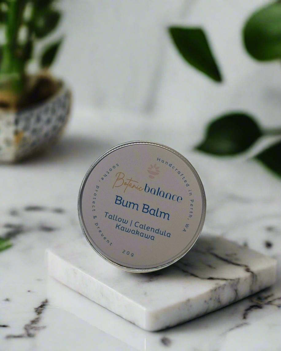 Bum balm container on a marble surface with greenery in the background
